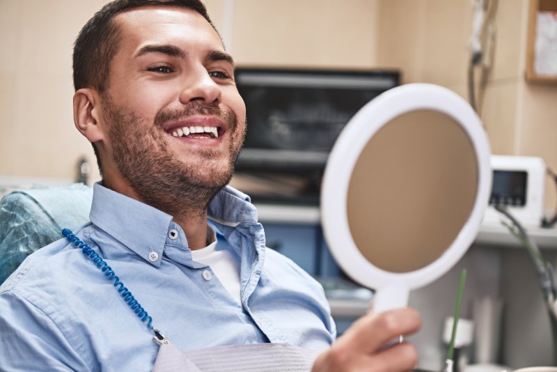 Male periodontal patient smiling and checking teeth in mirror