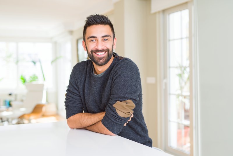 Man with dental implants leaning on table smiling